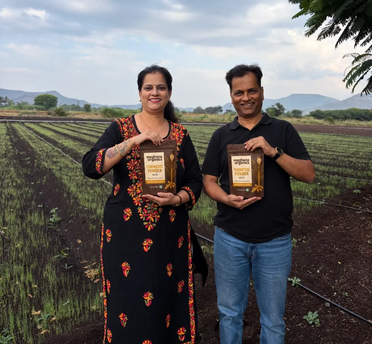 Our parents holding pouches of Meghana Organics turmeric powder in a farm field